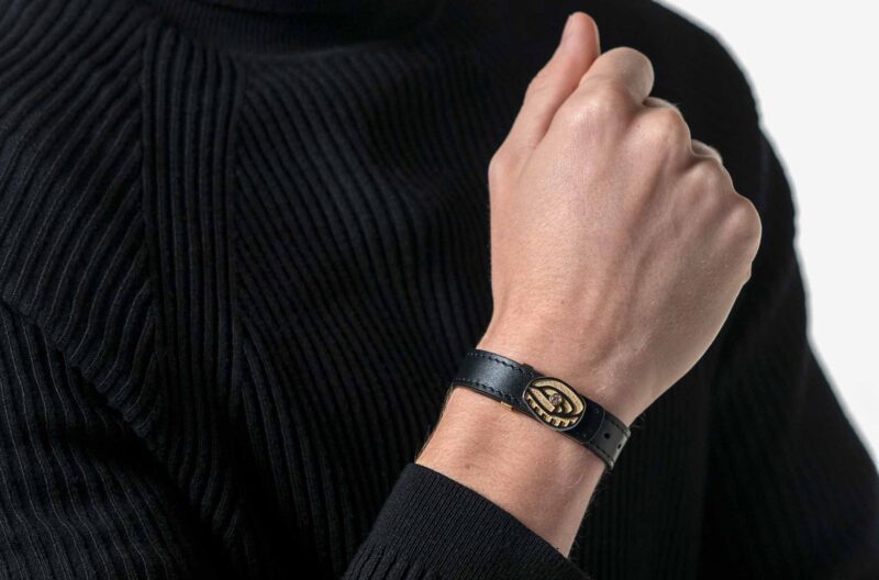 Modelo masculino con un suéter negro mostrando y luciendo la pulsera acabada en oro de 18K del FC Barcelona, con un diamante de 0.10 quilates engastado en su centro. Fondo blanco.