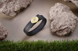La pulsera 1957 Oro, de elegante diseño de cuero genuino de color negro y bañada en oro, un verdadero emblema del Spotify Camp Nou. Rodeada de césped y piedras que reflejan su esencia, con un deslumbrante diamante en su centro.